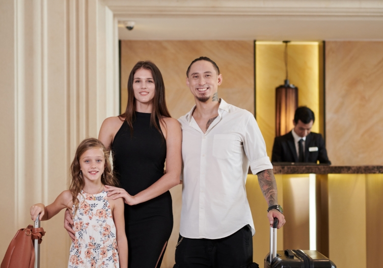 A family with luggage stands in front of a hotel, showcasing a kid-friendly resort in Myrtle Beach.