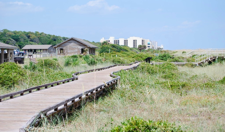 A scenic boardwalk extends to a beach and a house, showcasing the autism-friendly environment of Myrtle Beach State Park.