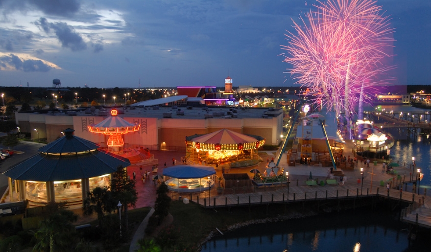A lively amusement park at night featuring a carousel and a fireworks display lighting up the sky.