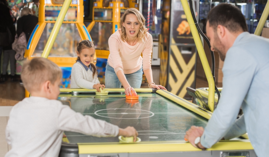A family engages in an exciting air hockey match in a game room, highlighting family-friendly fun at Dave & Buster’s, Myrtle Beach.