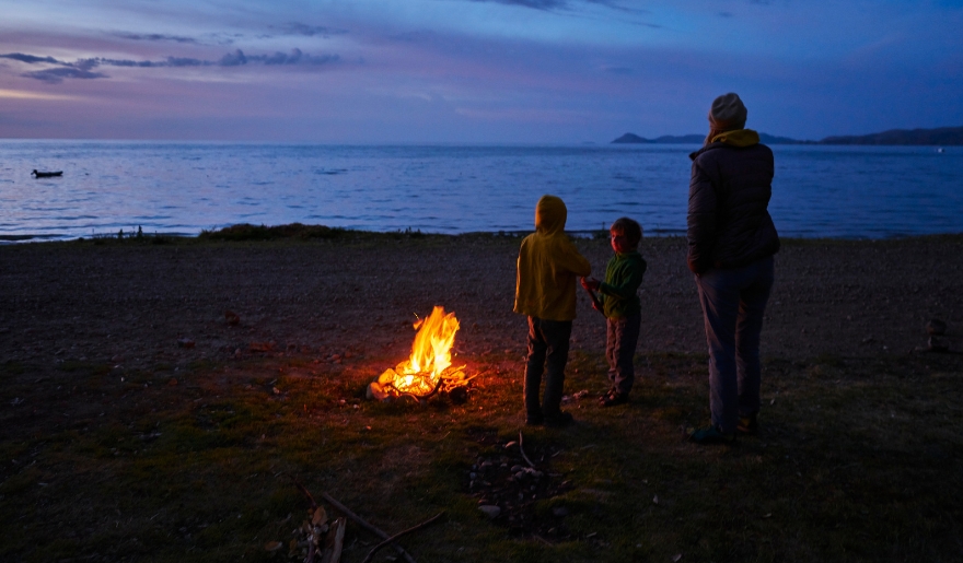A family gathers around a campfire on the beach at dusk, enjoying a cozy moment at Myrtle Beach's Grand Strand.