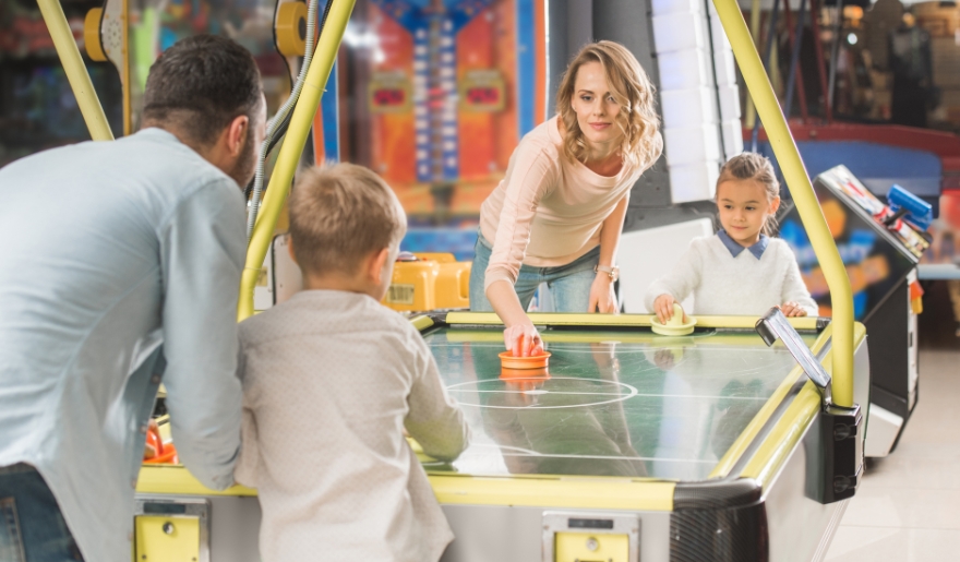 A family enjoys a game of air hockey together in a vibrant arcade at Myrtle Beach, surrounded by colorful game machines.
