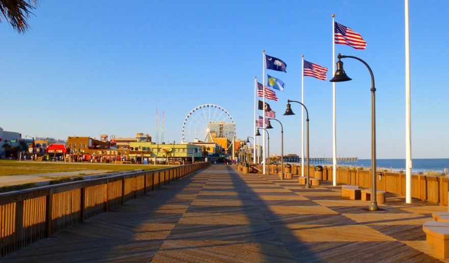 A lively scene of the Myrtle Beach boardwalk with fluttering flags and a prominent Ferris wheel, ideal for children's entertainment.