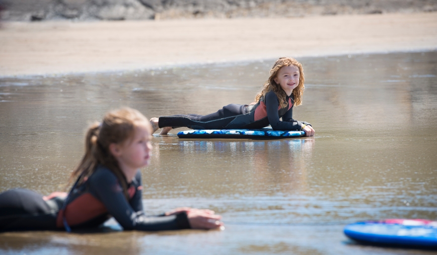 Two young girls lying on surfboards in the water, enjoying surf lessons at Myrtle Beach attractions for kids.