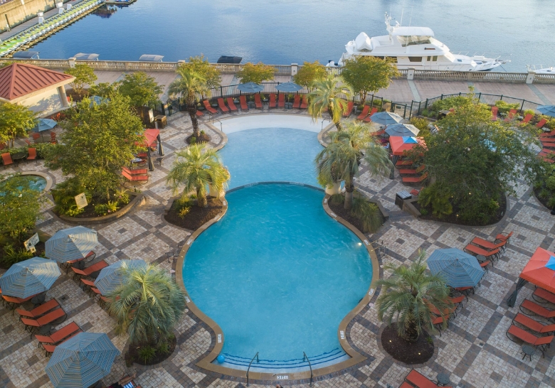 A pool with lounge chairs and umbrellas overlooks a marina at the Myrtle Beach Hotel for Large Groups.