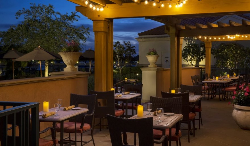 A nighttime view of a patio at WaterScapes Restaurant, featuring tables and chairs illuminated by soft lighting.