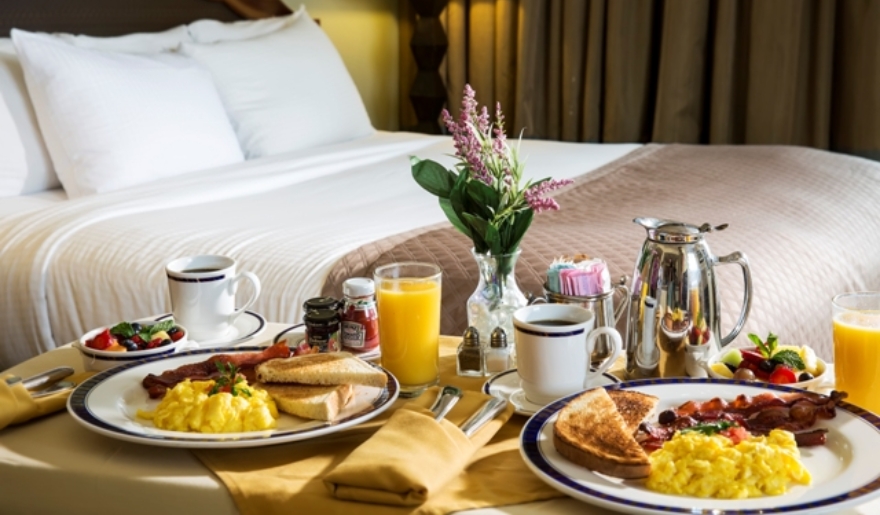 Breakfast in bed at Marina Inn, Myrtle Beach, featuring a cozy bed and a tray with coffee, pastries, and fruit.
