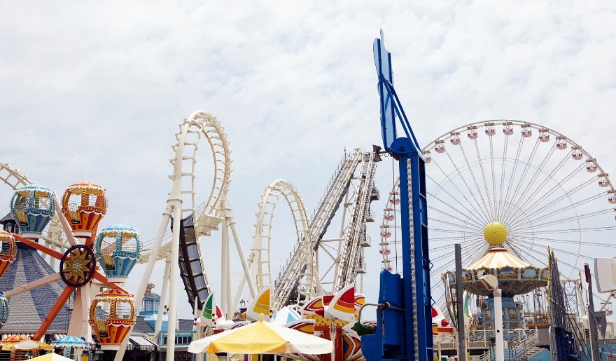 OD Pavilion Amusement Park scene with bright, colorful rides against a cloudy sky. Features Ferris wheel, roller coasters, and spinning ride evoking joy and excitement.