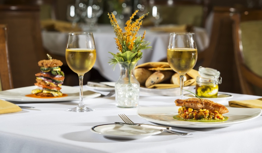 A restaurant table with two elegant dishes, glasses of white wine, at Marin Inn's Waterscapes Restaurant with cozy atmosphere part of Myrtle Beach golf packages.