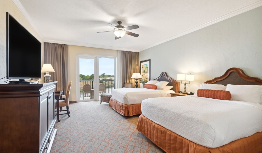 Two beds in a hotel room featuring a television and a balcony, part of family-friendly accommodations at Marina Inn near Myrtle Beach Water Parks.