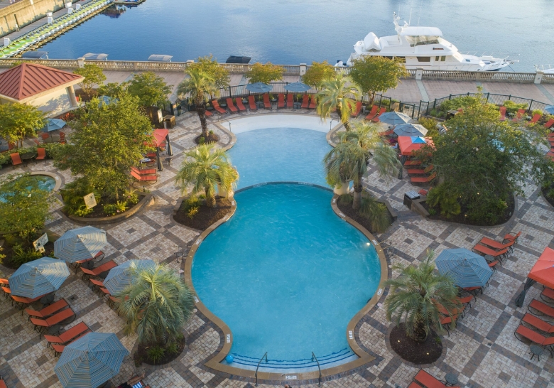 A pool with lounge chairs overlooks a serene body of water at a hotel near Myrtle Beach Sports Center.