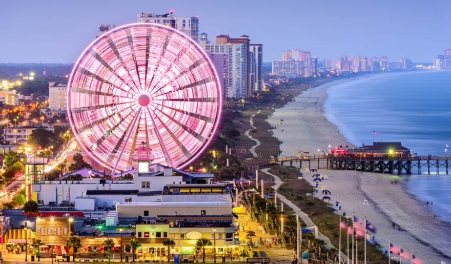 A brightly lit ferris wheel stands on Myrtle Beach at night, surrounded by festive decorations for Winter Wonderland in November.