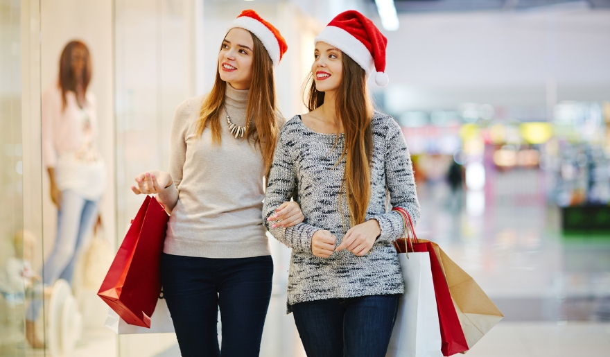 Two young women in festive Santa hats walk through a mall, celebrating the holiday season at Myrtle Beach's Broadway at the Beach.