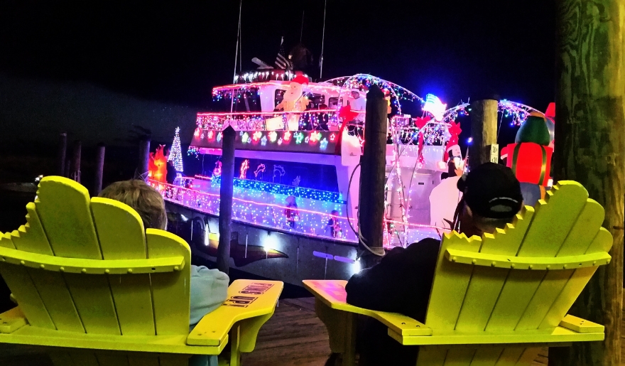 wo individuals seated in yellow chairs on a dock, observing a boat at the Myrtle Beach Christmas Intracoastal Regatta.