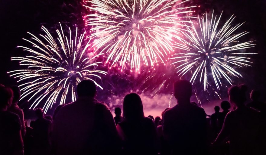 A crowd gathers at Broadway at the Beach, watching colorful fireworks illuminate the night sky during New Year’s celebrations.