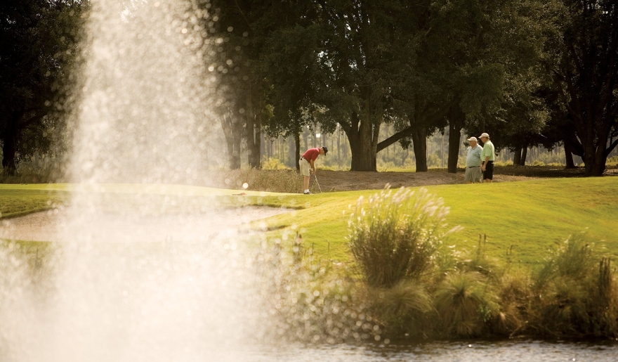 A group of people plays golf near a fountain at Myrtle Beach, celebrating Thanksgiving on the golf course.