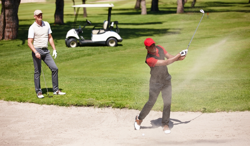 Two men engaged in a golf game in the sand, representing Myrtle Beach's golfing experience and seasonal travel tips.