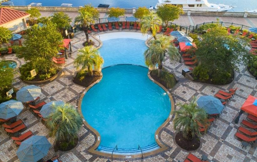A pool with lounge chairs overlooks a serene body of water at a hotel near Myrtle Beach Sports Center.