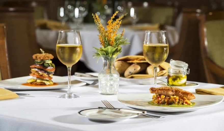 A table at Myrtle Beach in April, adorned with two plates of food and two glasses of wine for a dining experience.