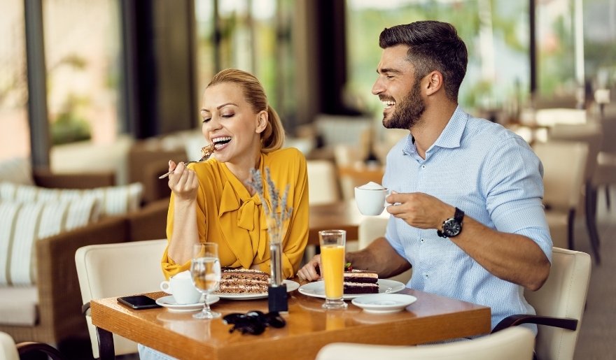 Couple enjoying breakfast with cake, coffee, and juice at a cozy restaurant table