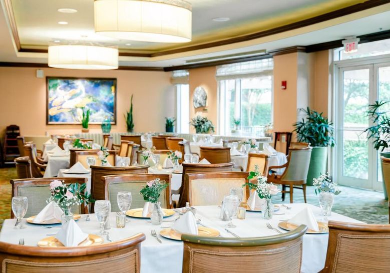 An elegant hotel dining room set up with multiple tables, white linens, and floral centerpieces.