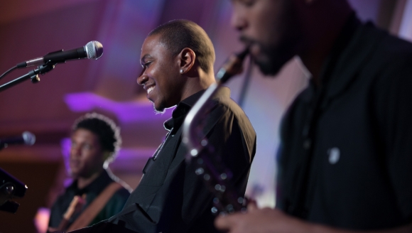 Three musicians performing jazz on stage with a smiling saxophonist in focus.