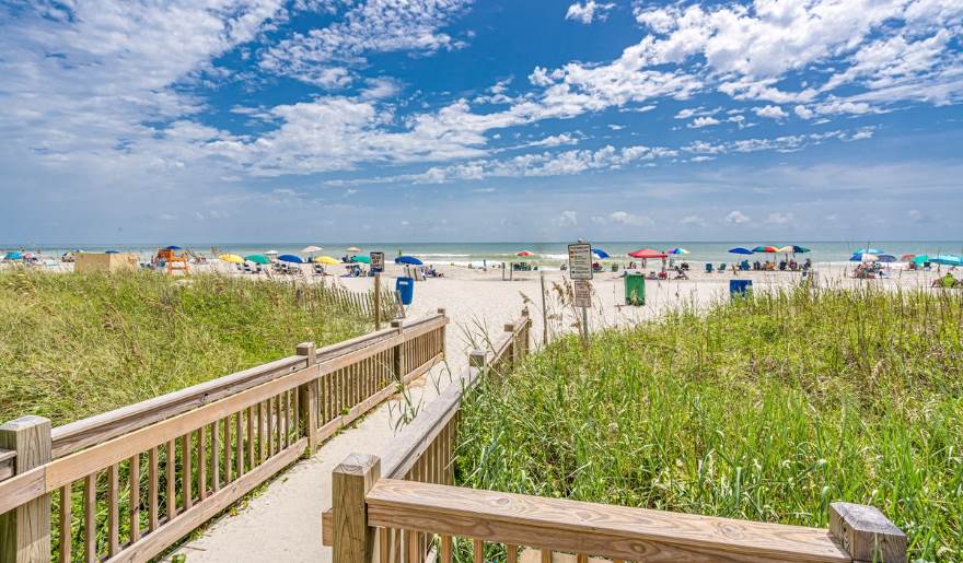A wooden walkway leads through grass to the beach, highlighting the best time to visit Myrtle Beach for travelers.