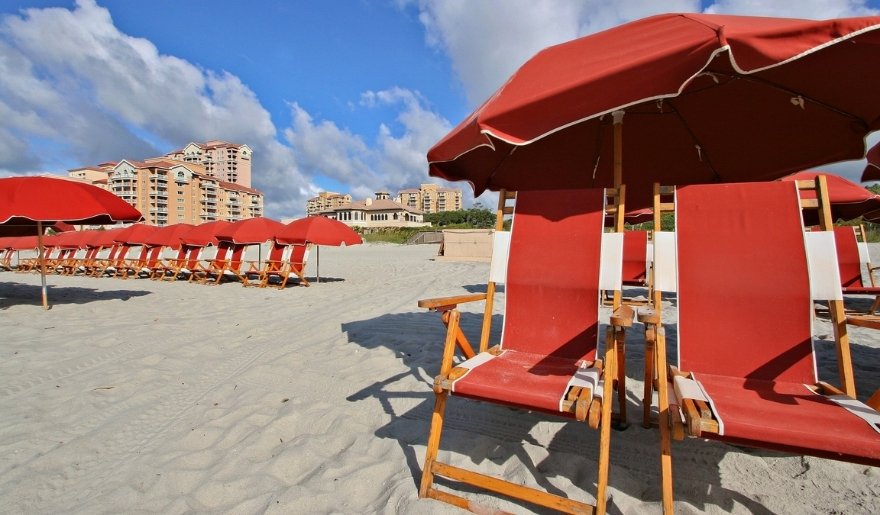 Red beach chairs lined along Myrtle Beach shoreline under sunny coastal skies