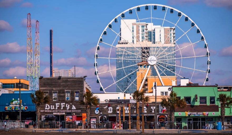 The Myrtle Beach SkyWheel building is visible behind a vibrant Ferris wheel at Myrtle Beach Amusement Parks.