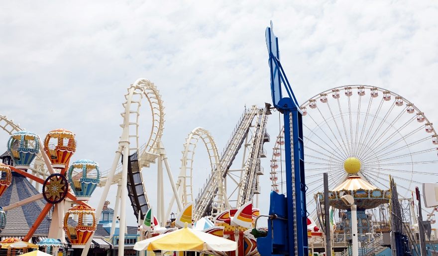 OD Pavilion Amusement Park scene with bright, colorful rides against a cloudy sky. Features Ferris wheel, roller coasters, and spinning ride evoking joy and excitement.