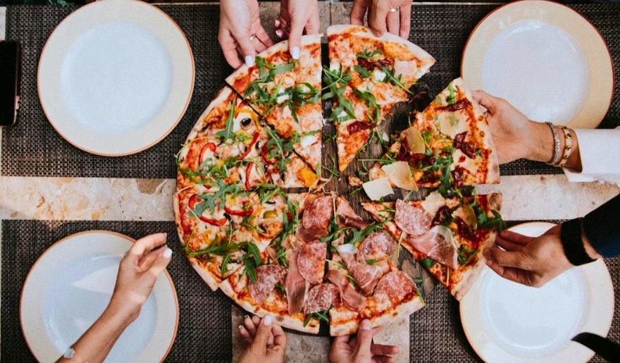 A joyful group of individuals holding hands around a pizza, celebrating together at Ultimate California Pizza Game Zone.
