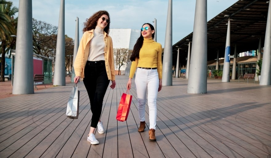 Two women stroll down a sidewalk at Barefoot Landing in Myrtle Beach, each carrying shopping bags.
