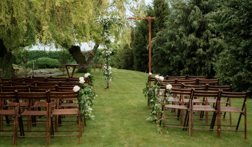 Outdoor wedding ceremony at Silver Coast Winery, featuring wooden chairs set beneath a graceful willow tree.