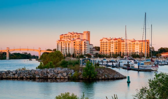 A scenic view of a waterfront resort complex next to a bridge and a boat marina at dusk.