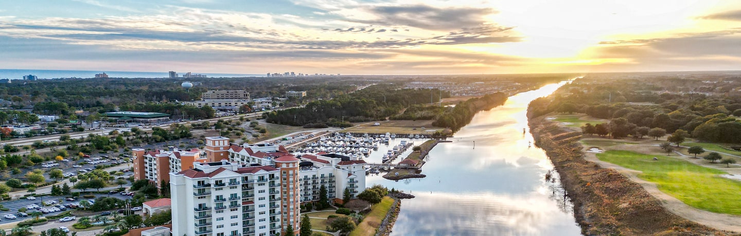 An aerial panoramic view of a resort and marina along a calm river at sunrise.
