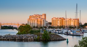 A sunset view of a waterfront hotel resort with docked sailboats and a bridge.