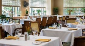 An elegant restaurant dining room featuring tables with white tablecloths and yellow napkins.