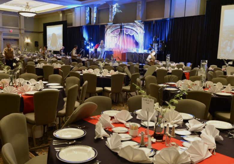 A large banquet hall set up with many dining tables, a stage, and projection screens.