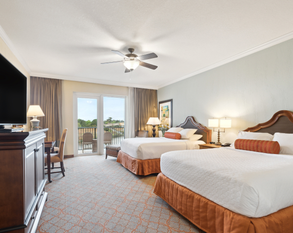 A hotel room with two queen beds, orange accents, a TV console, and a balcony view.