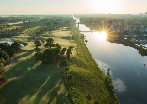 Aerial view of a green golf course next to a river reflecting a bright sunrise.